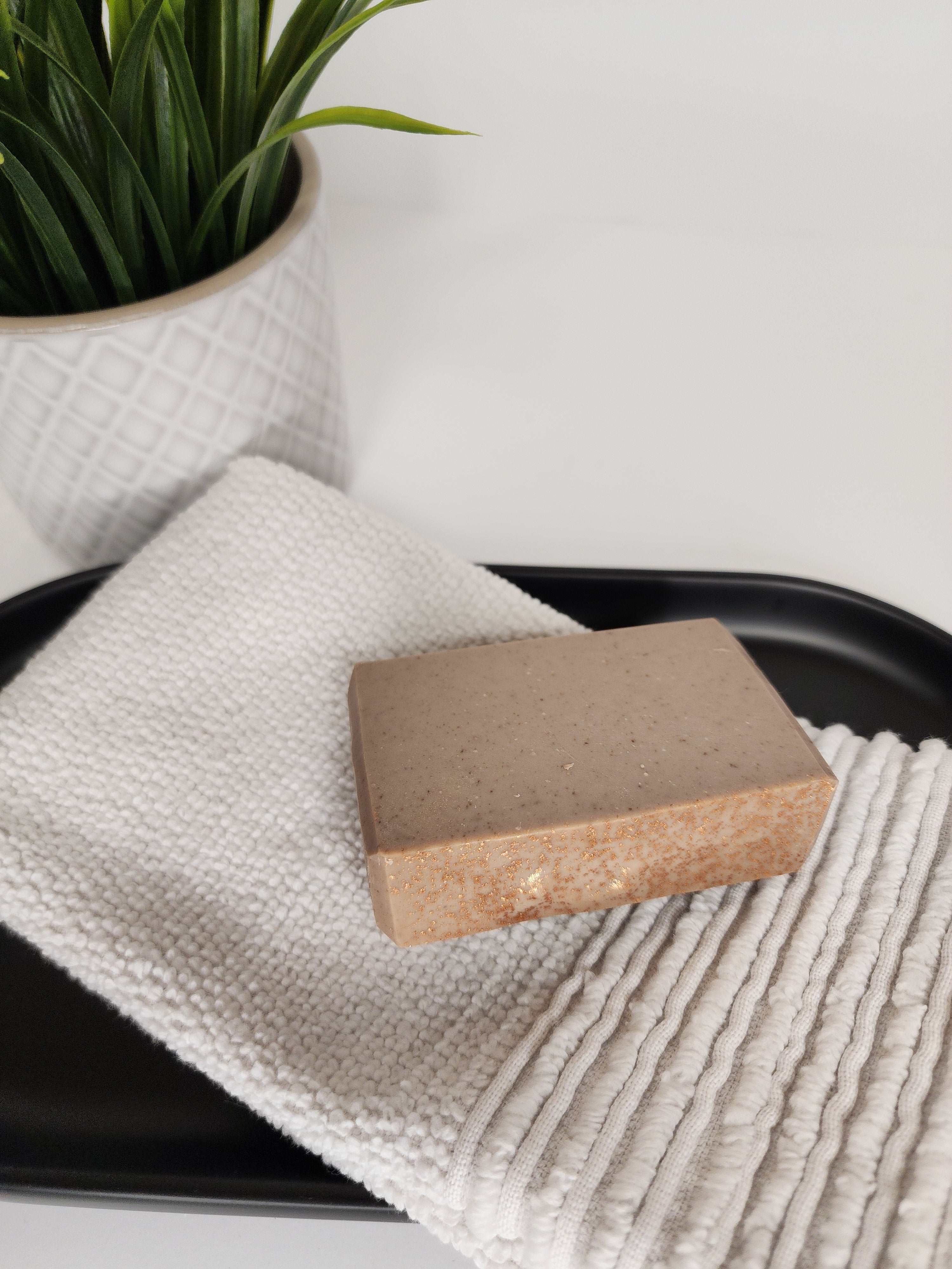 A tan bar of Vanillawood handmade goat milk soap with copper glimmer on a fluffy grey towel