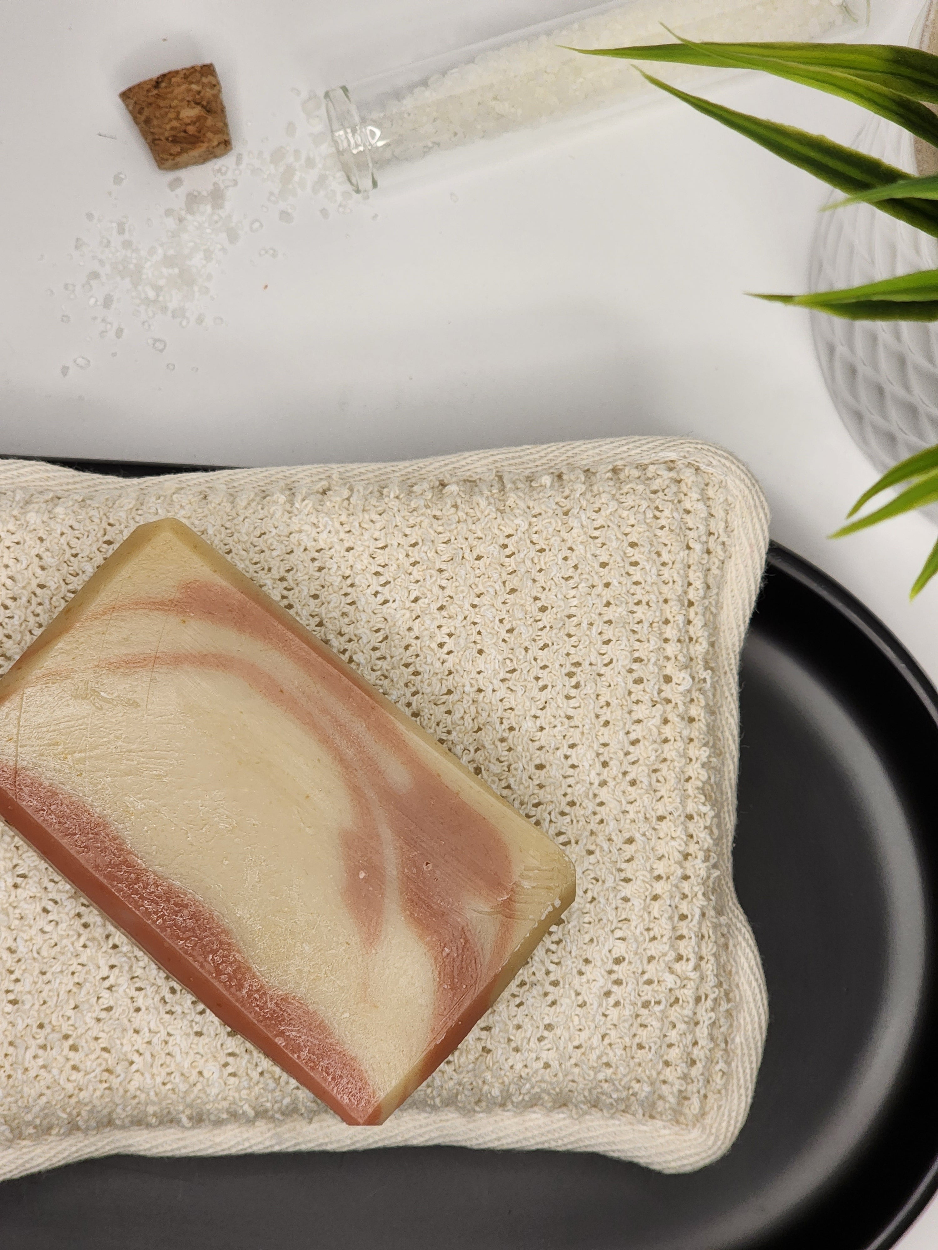 A raspberry and naturally colored bar of Berry Rhubarb goat milk soap atop an exfoliating sponge