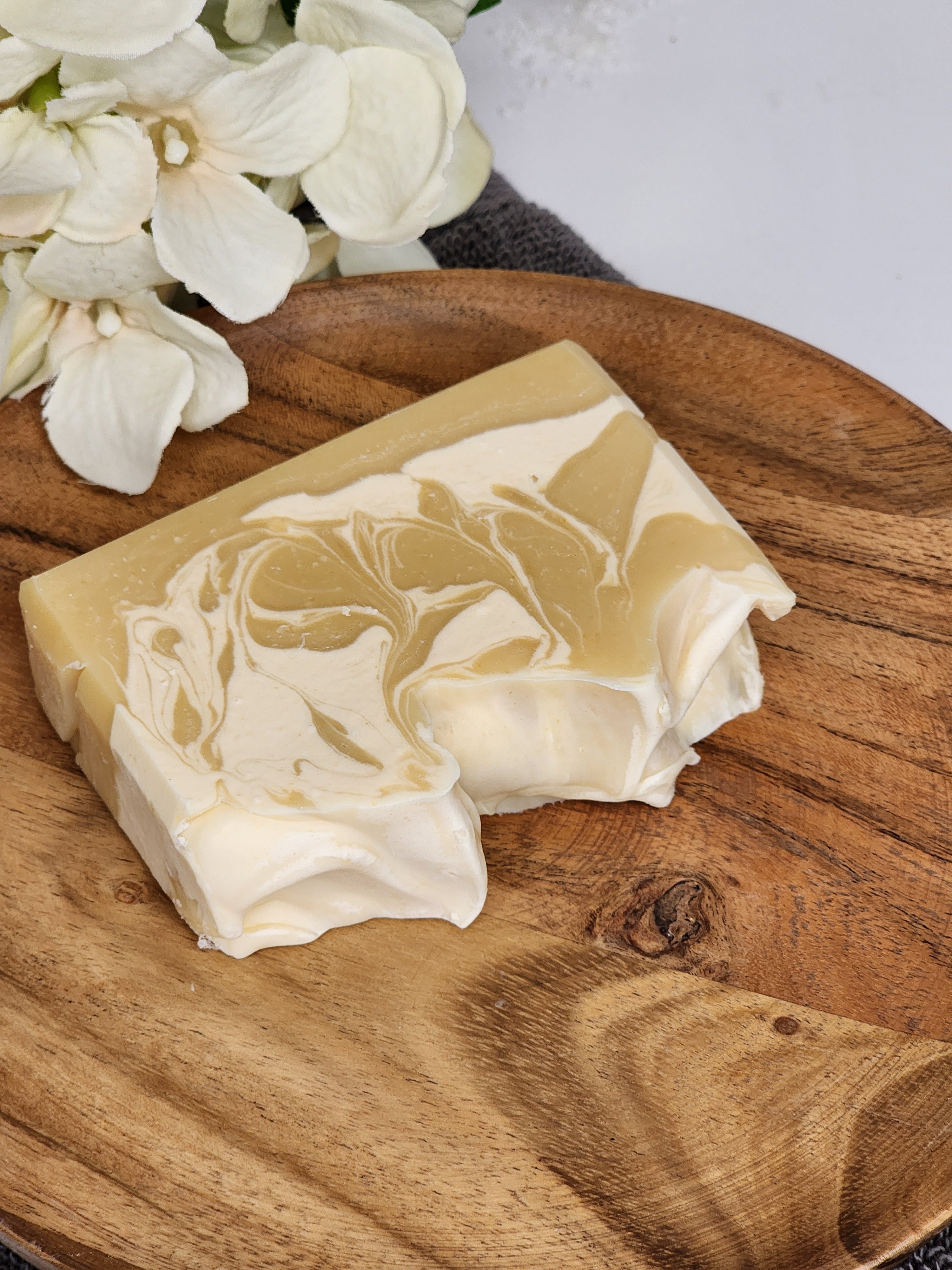 A naturally and white colored bar of handmade lemon and patchouli soap on a wooden platter